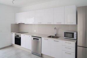 Eine moderne Küche mit weißen Schränken, einem Geschirrspüler, einer Spüle, einer Mikrowelle und einem Edelstahl-Kühlschrank.