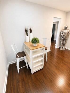 Un petit coin repas avec une table blanche, deux chaises, une plante en pot et une figurine décorative en métal.