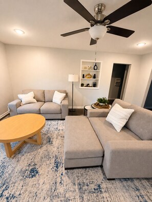 A living room with a sofa, a coffee table, a floor lamp, and a ceiling fan.