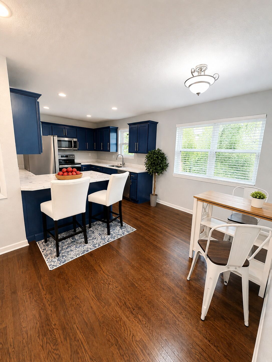 Une cuisine moderne avec des meubles de couleur bleu foncé, un réfrigérateur en acier inoxydable et une table à manger en bois, assortie de chaises blanches.