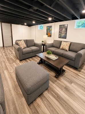 Un salon moderne avec deux canapés gris, une table basse en bois et un pouf gris.
