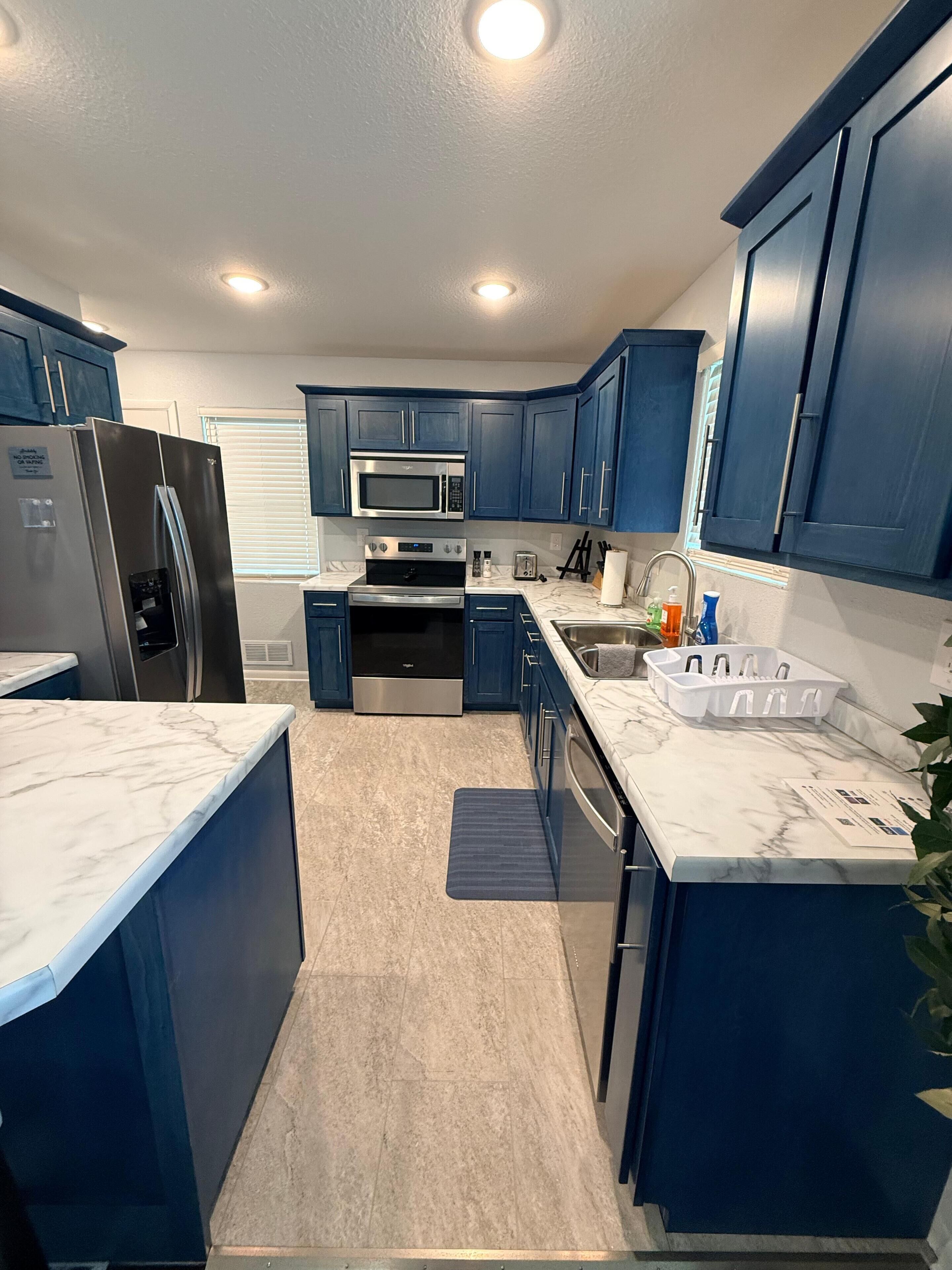 Une cuisine moderne avec des meubles bleu foncé, des appareils en acier inoxydable et un plan de travail en marbre.