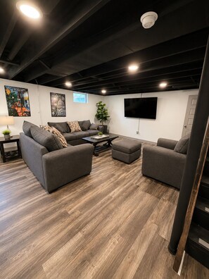 Un salon moderne avec un canapé gris, une table basse et un téléviseur à écran plat fixé au mur.