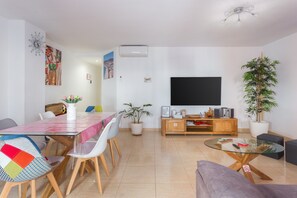 Uma sala de estar moderna com uma mesa de jantar, cadeiras, um sofá, televisão e plantas em vasos.