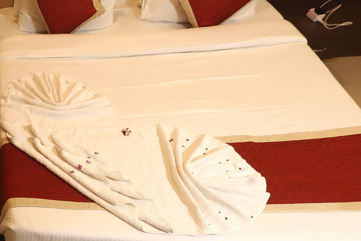 A neatly made bed with a red and white color scheme, a folded towel, and a decorative pillow.