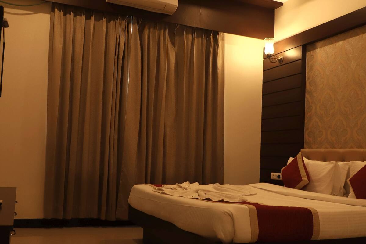 A hotel room with a bed, curtains, a wall-mounted light, and a patterned wallpaper.