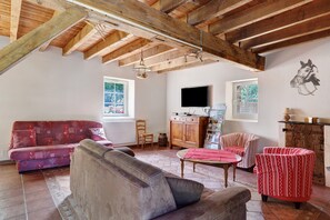 A rustic living room with exposed wooden beams, a sofa, a coffee table, a TV, and a horse mural on the wall. - Gîte Le Relais Des Hirondelles: Lake View, Private Terrace & Wi-Fi (Segré-en-Anjou Bleu)