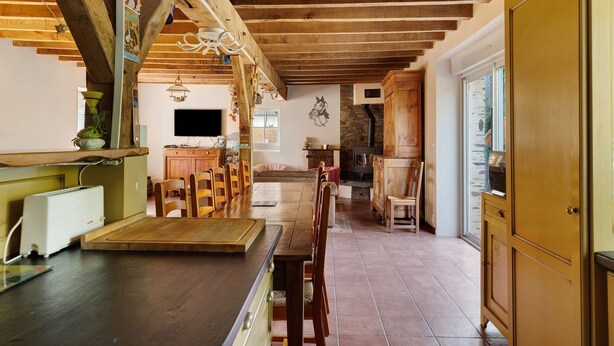 A rustic kitchen with wooden beams, a dining table, chairs, and a television. - Gîte Le Relais Des Hirondelles: Lake View, Private Terrace & Wi-Fi (Segré-en-Anjou Bleu)