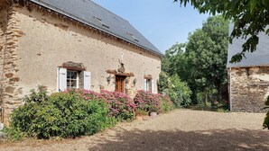 A stone building with a gravel driveway, a wooden door, and a window with shutters. - Gîte Le Relais Des Hirondelles: Lake View, Private Terrace & Wi-Fi (Segré-en-Anjou Bleu)