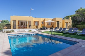 A swimming pool with lounge chairs, a covered seating area, and a building with a yellow facade.