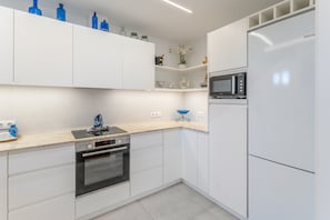 A modern kitchen with white cabinetry, a built-in oven, a microwave, and a sink.