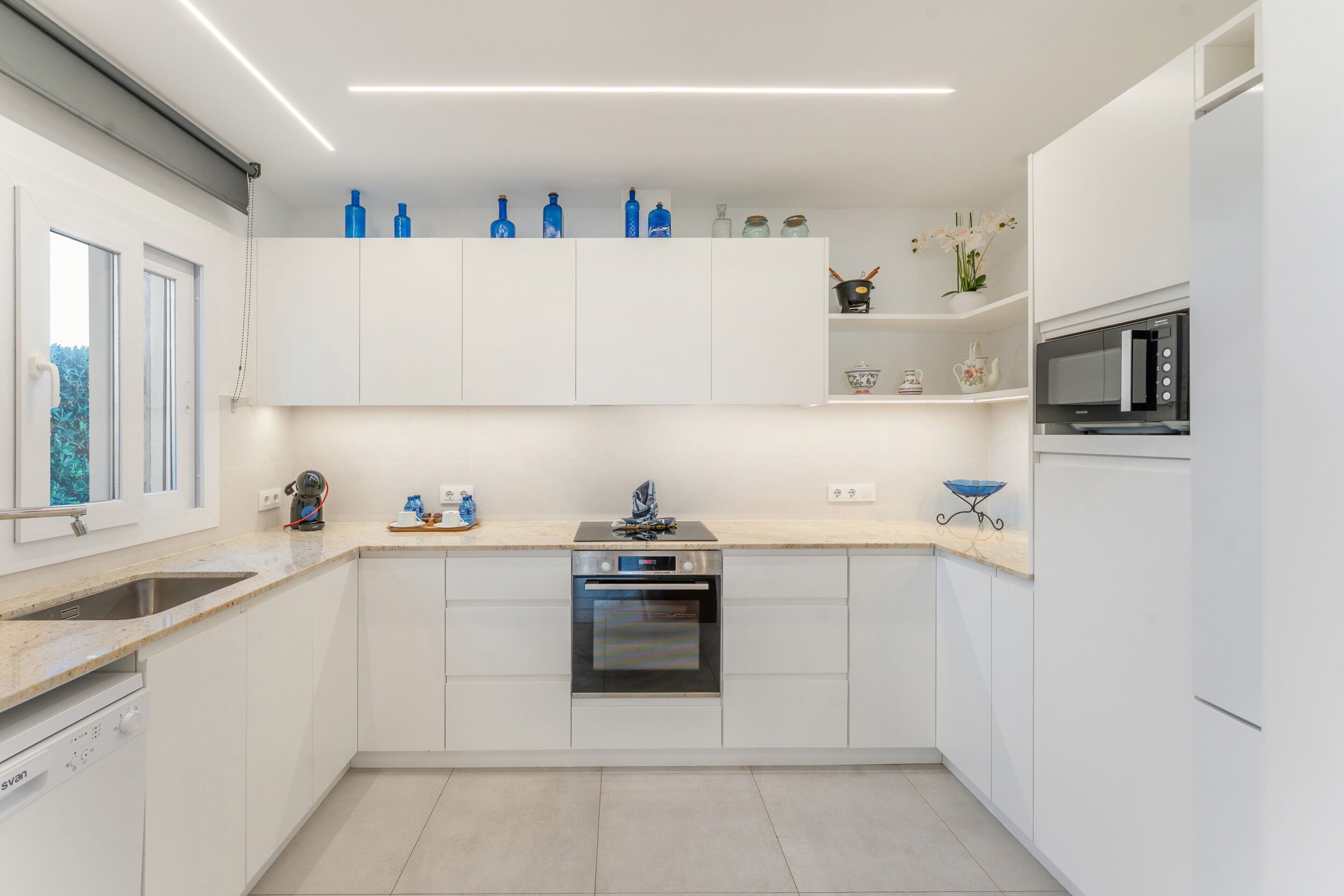 A modern kitchen with white cabinetry, a built-in oven, a microwave, and a window with a view of greenery.