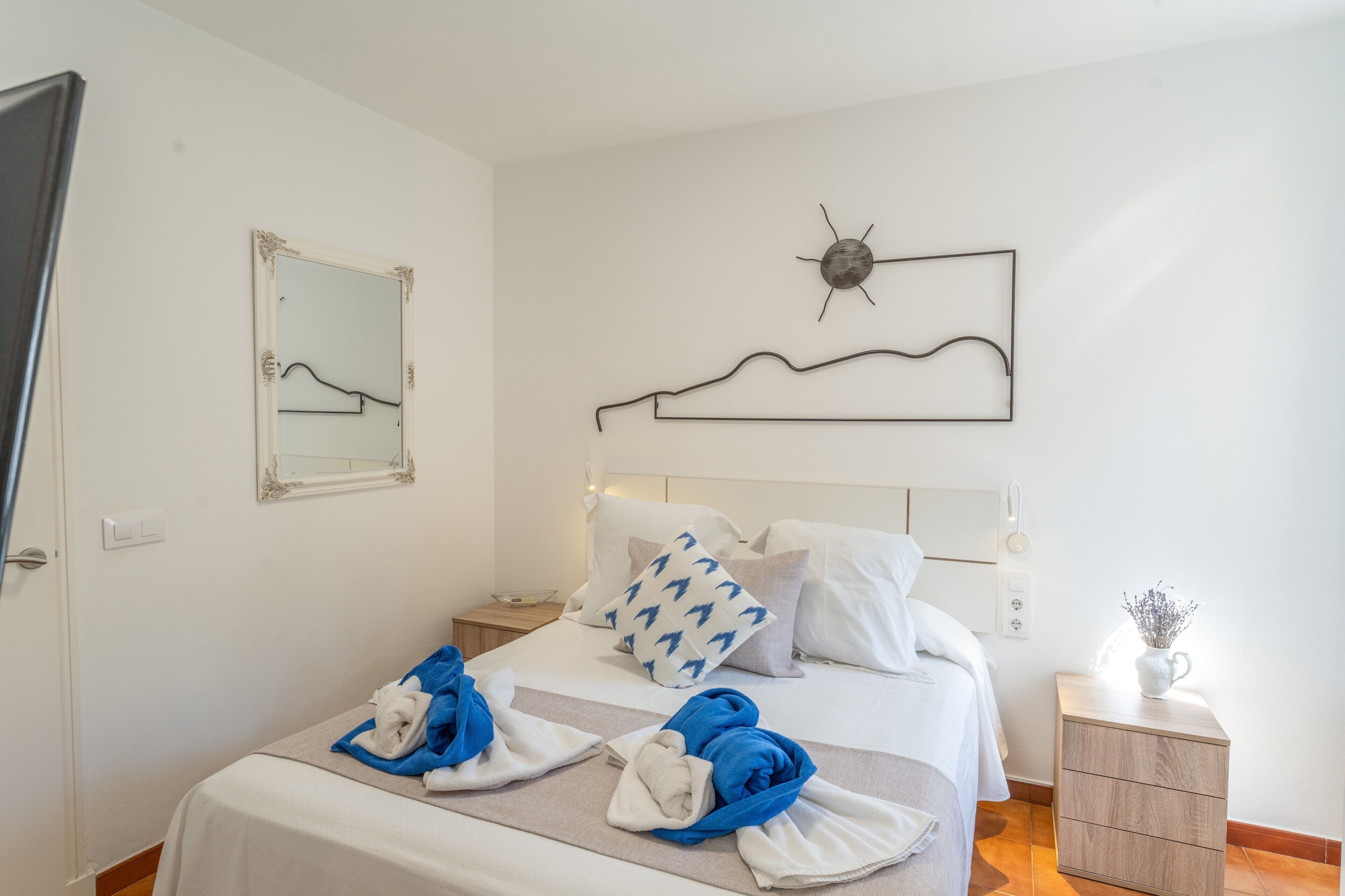 A bedroom with a bed, a nightstand, a wall clock, and a mirror.