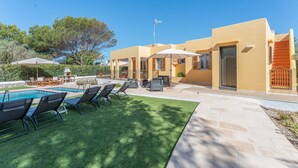 Zona de piscina amb gandules, un patio i un edifici amb teulada plana i grans finestres.