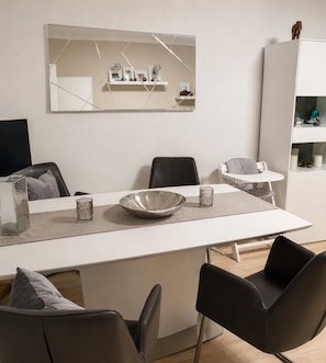 Un espace repas moderne avec une table blanche, des chaises noires et un grand miroir au-dessus.