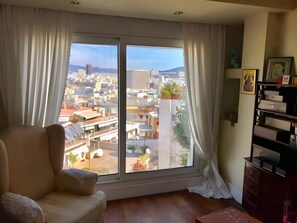A room with a large window, a sofa, a wooden floor, and a bookshelf. - Luxury Penthouse with Private Pool, Terrace, and Stunning Views (Athens)