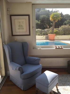 A room with a large window, a blue armchair, a small ottoman, a radiator, and a framed picture on the wall. - Luxury Penthouse with Private Pool, Terrace, and Stunning Views (Athens)