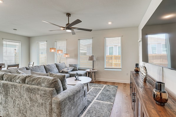 A modern living room with a sectional sofa, a coffee table, a floor lamp, and a ceiling fan.