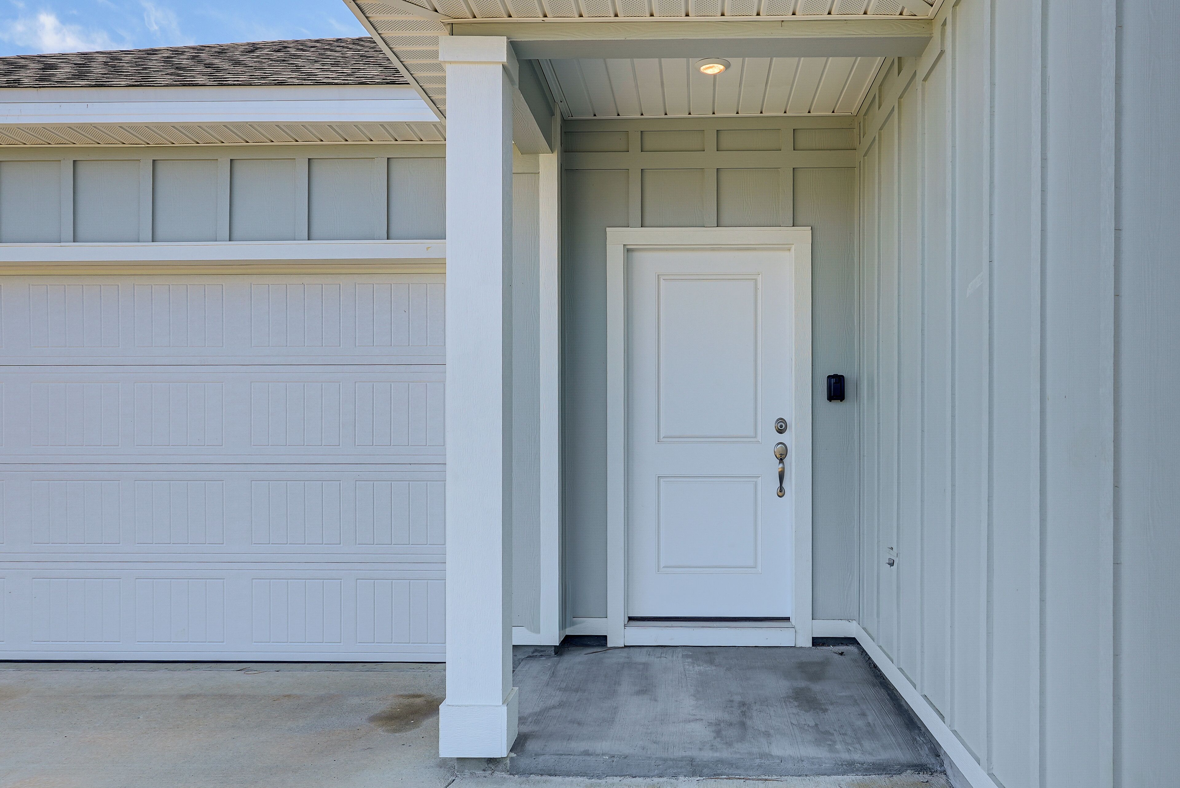 A garage door, a white door with a handle, and a concrete step leading to a porch.