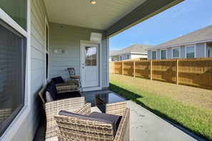 A covered porch with wicker furniture, a door, and a view of a fenced backyard.