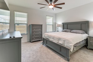 A bedroom with a bed, dresser, nightstand, ceiling fan, and windows.
