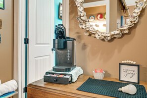 Eine Kaffeemaschine auf einer Holzauslage, ein gerahmtes, motivierendes Zitat, eine Glühbirne und ein dekorativer Spiegel mit Bordüre aus Austernschalen.