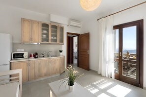 Eine moderne Küche mit Holzausstattung, einer Mikrowelle und einer Kaffeemaschine. Es gibt einen Essbereich mit Tisch und Stühlen sowie einen Balkon mit Aussicht.