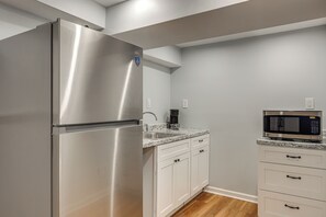 Eine Küche mit Edelstahl-Kühlschrank, Mikrowelle, einer Arbeitsplatte aus Granit und weißen Schränken.