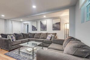 Ein modernes Wohnzimmer mit einer Eckcouch, einem Glastisch und Wandbildern.