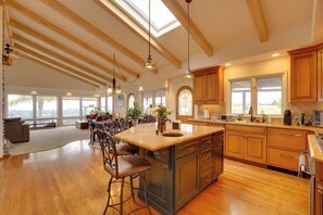 A spacious kitchen with wooden cabinets, a large island, and a dining area with chairs and a table. - Ocean View + Private Garden: Santa Cruz Home (Santa Cruz)