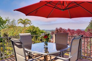 A round glass table with metal chairs and a red umbrella, set on a balcony with a view of trees and hills. - Ocean View + Private Garden: Santa Cruz Home (Santa Cruz)