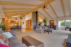 A spacious living area with a high ceiling, a stone fireplace, and a dining area with wooden furniture. - Ocean View + Private Garden: Santa Cruz Home (Santa Cruz)