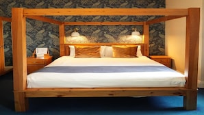 Een hemelbed met een houten frame, wit beddengoed en twee bedlampjes.