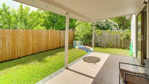 A covered patio with a trampoline, a wooden fence, and a grassy yard. - Satx Family Getaway w/ Patio, Grill & Yard! (San Antonio)