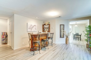 A dining area with a wooden bar and chairs, a bookshelf, a framed picture, and a mirror.