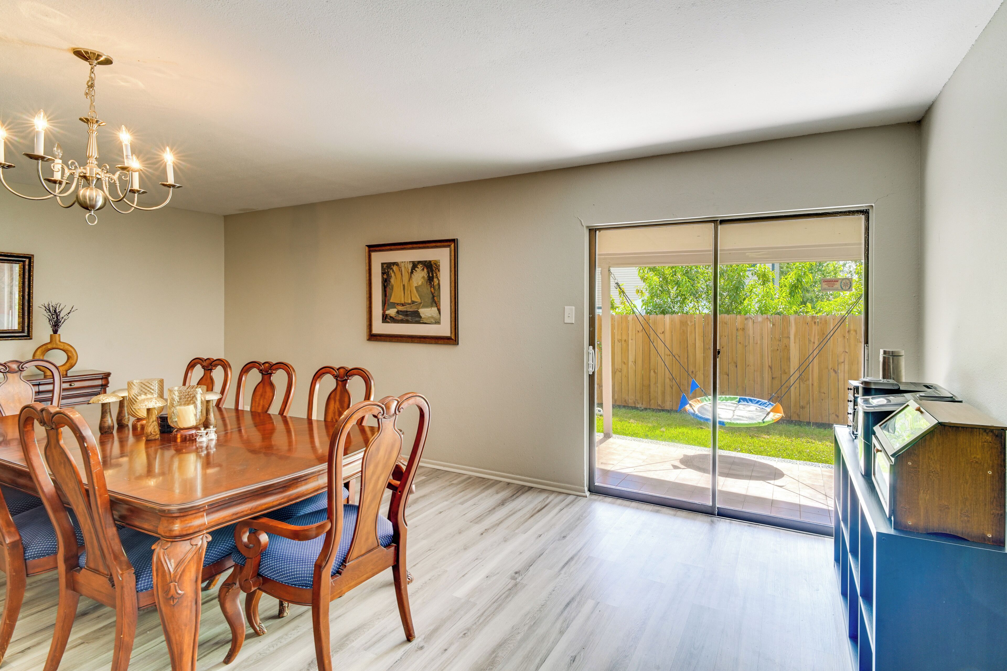 A dining area with a wooden table and chairs, a chandelier, and a sliding glass door leading to a backyard.