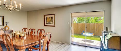 A dining area with a wooden table and chairs, a chandelier, and a sliding glass door leading to a backyard.
