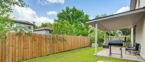 A backyard with a wooden fence, a grill, and a covered patio area.