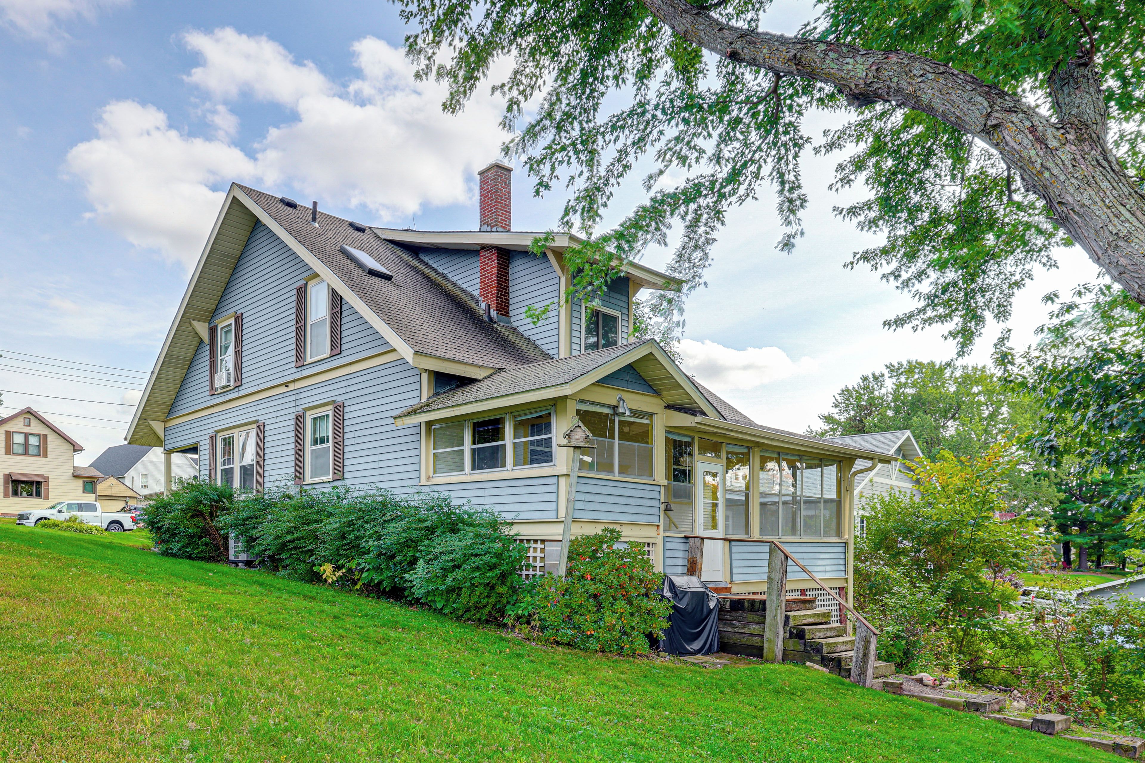 A two-story house with a steeply pitched roof, a chimney, and a covered porch with steps leading to a deck.
