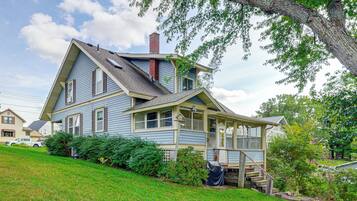 A two-story house with a steeply pitched roof, a chimney, and a covered porch with steps leading to a deck.