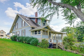 A two-story house with a steeply pitched roof, a chimney, and a covered porch with steps leading to a deck. - Historic Home on Beaver Dam Lake w/ Seasonal Dock (Cumberland)