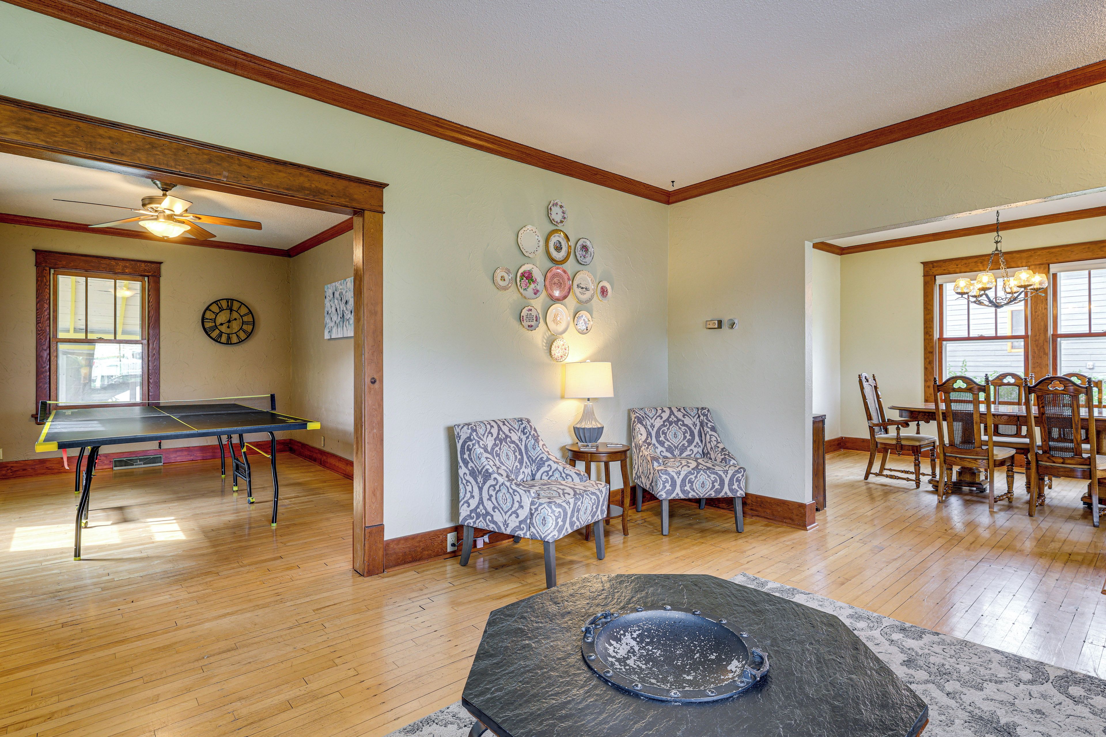 A spacious living room with a ping pong table, two patterned armchairs, a dining area with wooden chairs, and a stone coffee table.