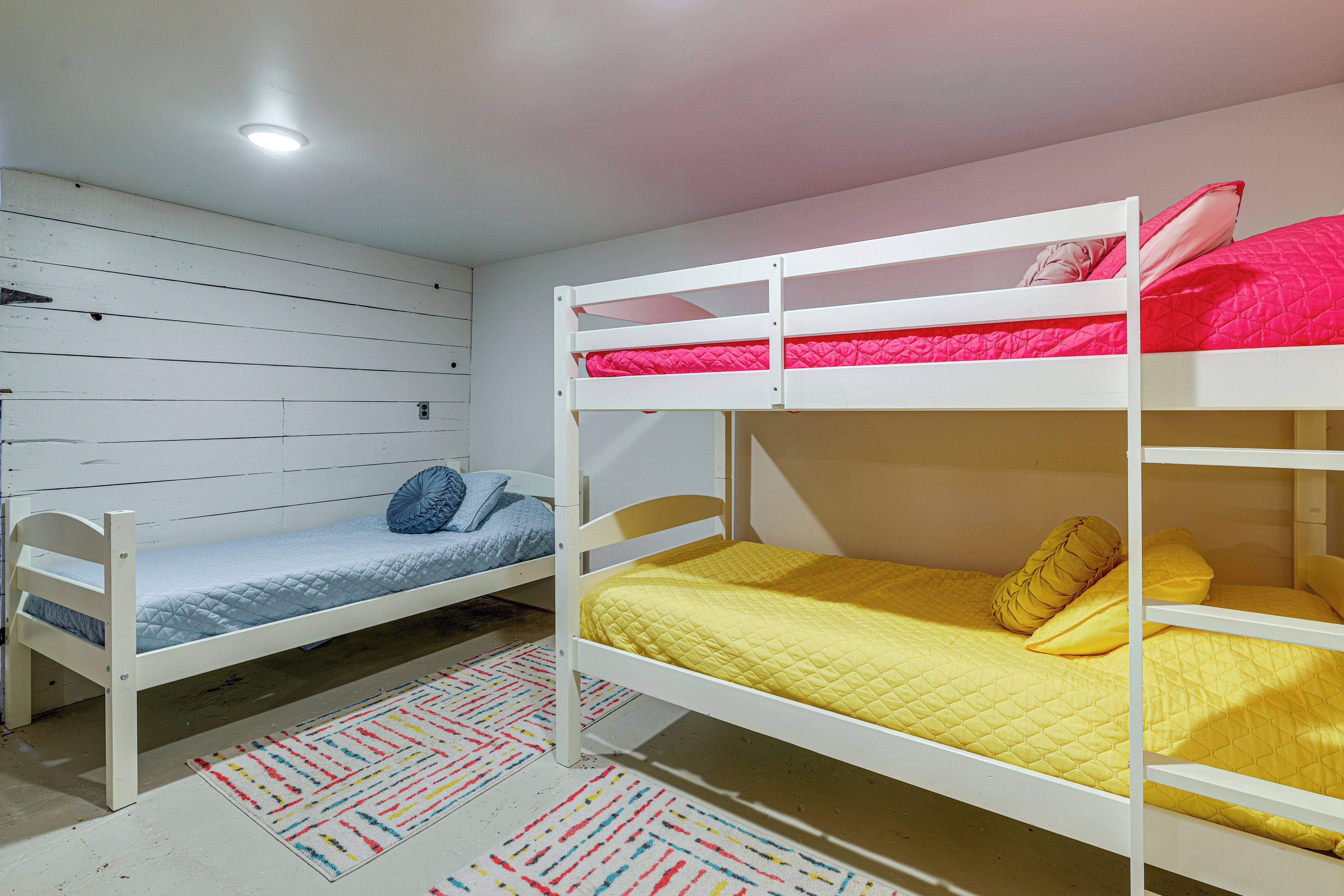 A bunk bed room with a lower bunk and a single bed, a colorful rug, and a white ceiling with a light fixture.