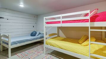 A bunk bed room with a lower bunk and a single bed, a colorful rug, and a white ceiling with a light fixture.