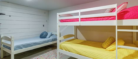 A bunk bed room with a lower bunk and a single bed, a colorful rug, and a white ceiling with a light fixture.