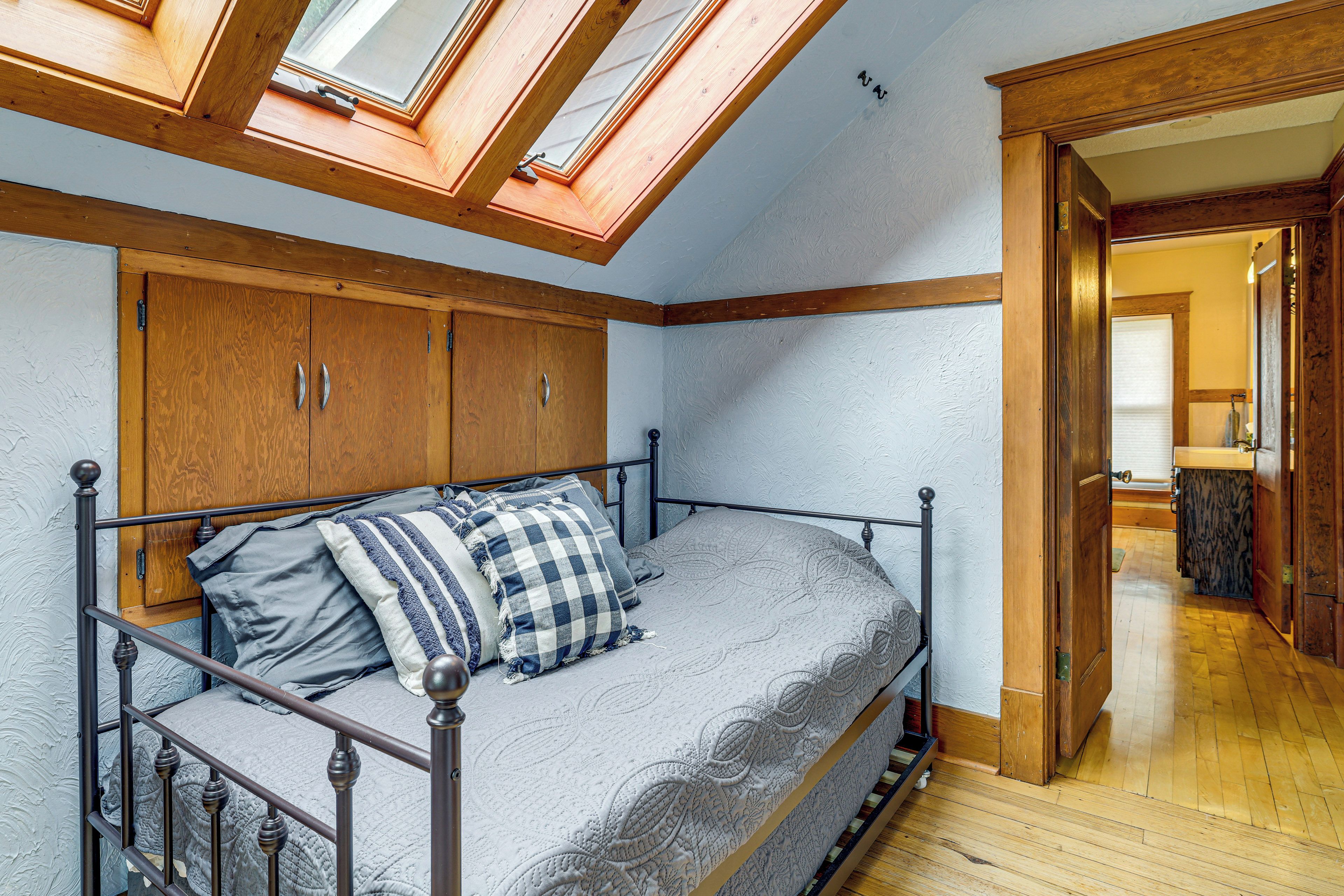 Une chambre avec un puits de lumière, une armoire en bois et un lit avec des oreillers.