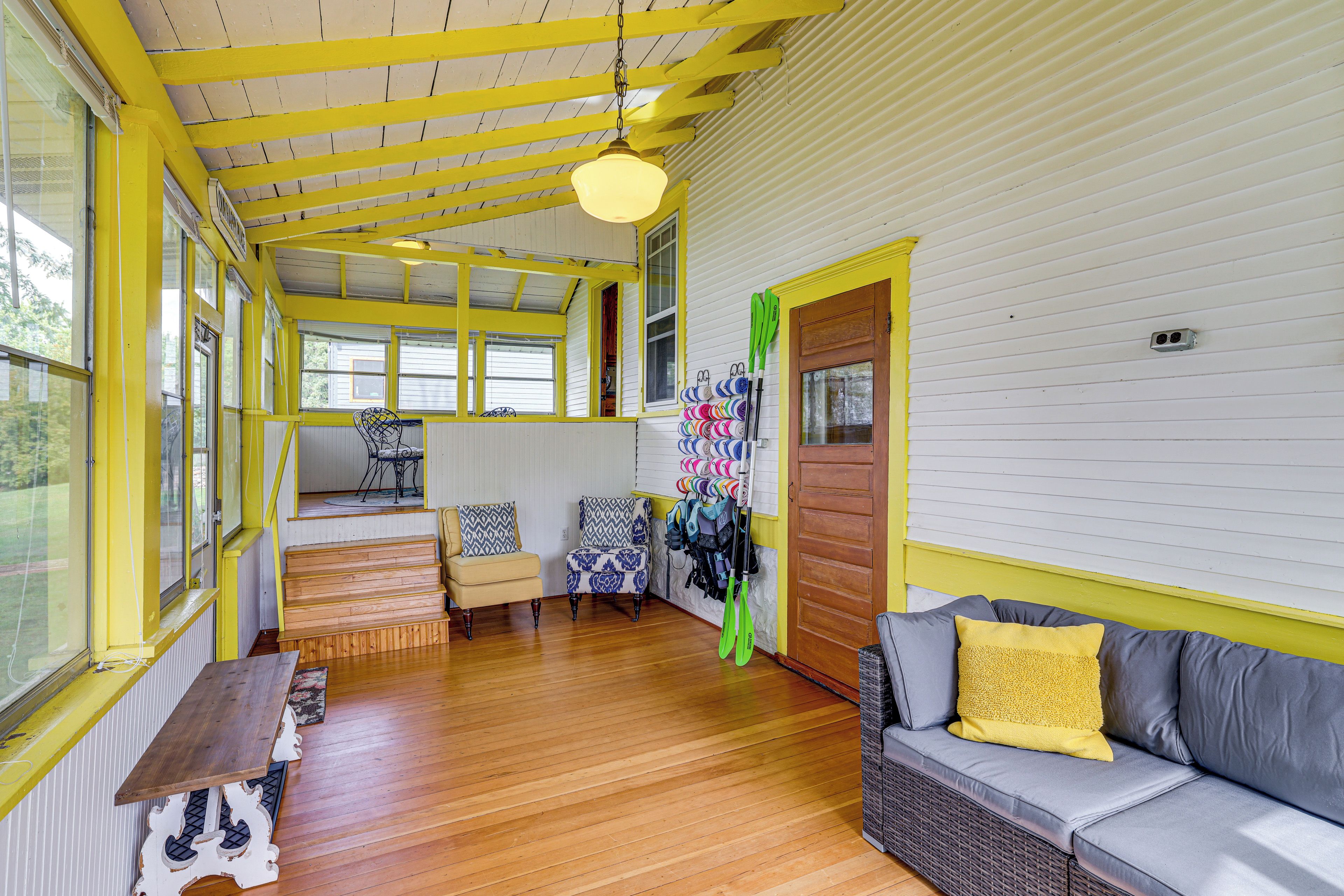 A room with wooden floors, a sofa with a yellow pillow, a chair, a table, and a wall with a door.