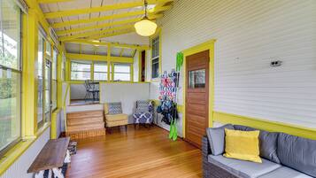 A room with wooden floors, a sofa with a yellow pillow, a chair, a table, and a wall with a door.