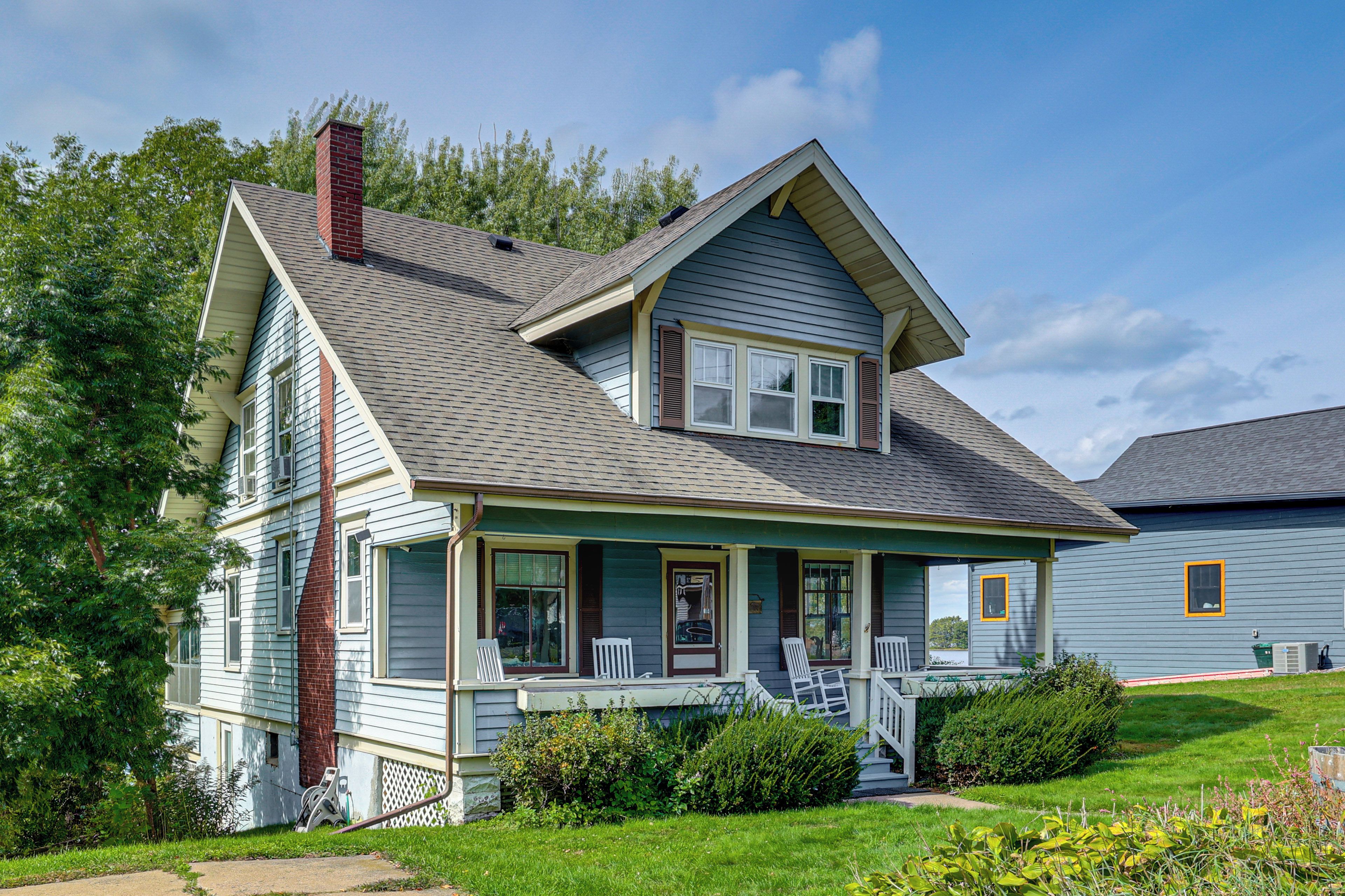 A two-story house with a gabled roof, a front porch with white railings, and a brick chimney.