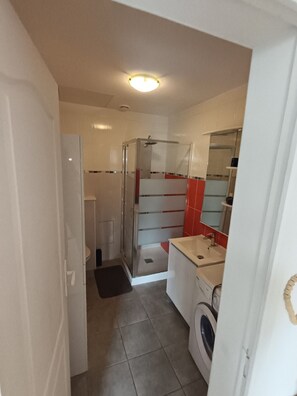 Ein kleines Badezimmer mit Dusche, Toilette und Waschmaschine.